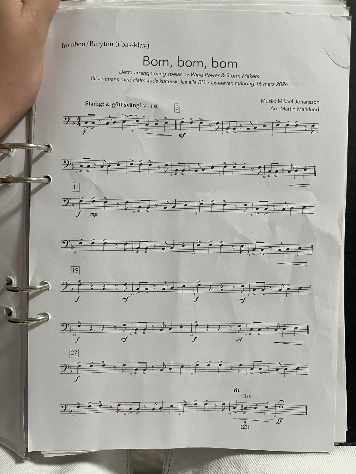 A trombone part photographed in a ring binder, page curled and shadowed